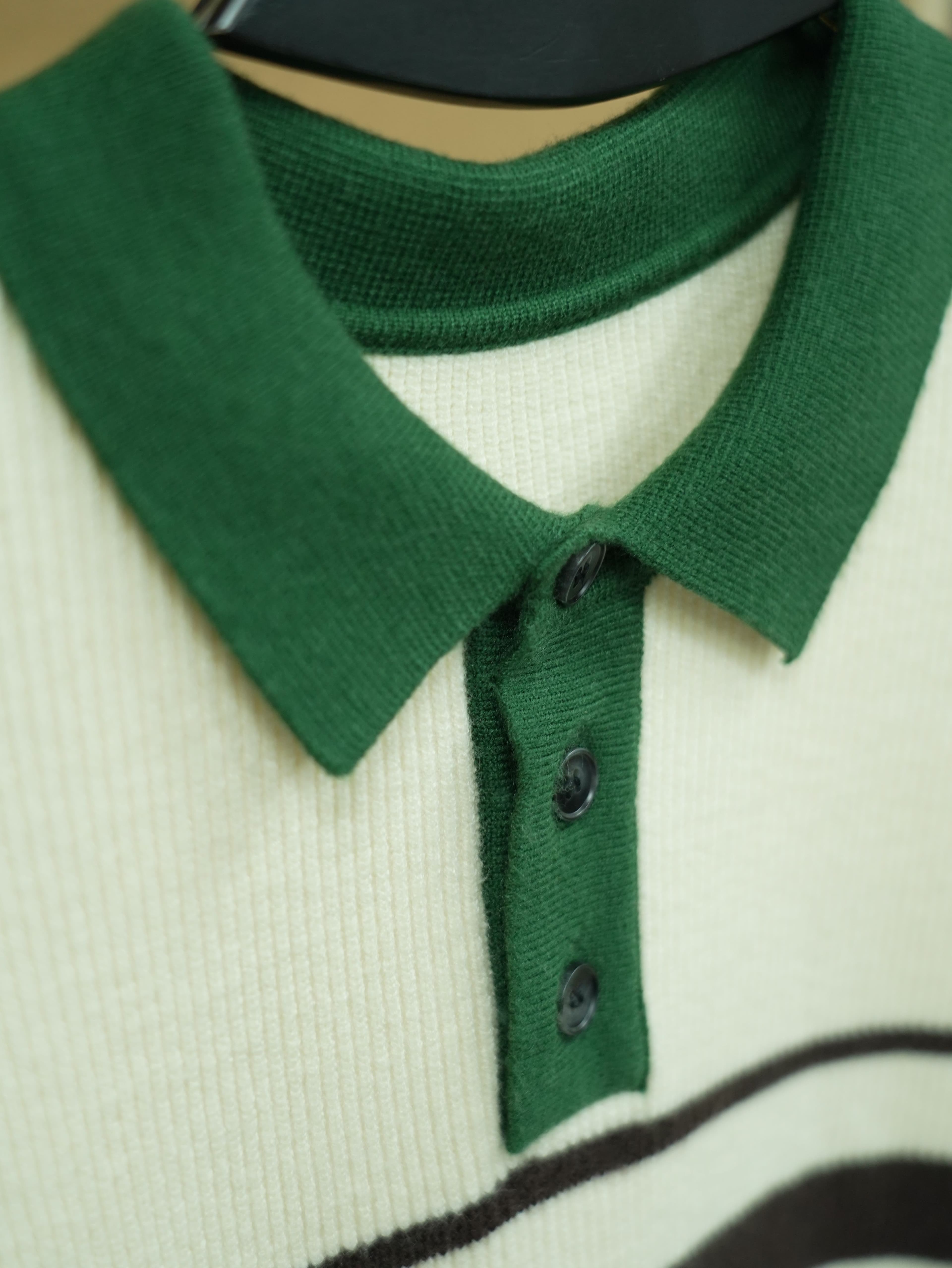 Close-up of an ivory rib-knit polo with a forest-green collar and button placket for a smart-casual capsule